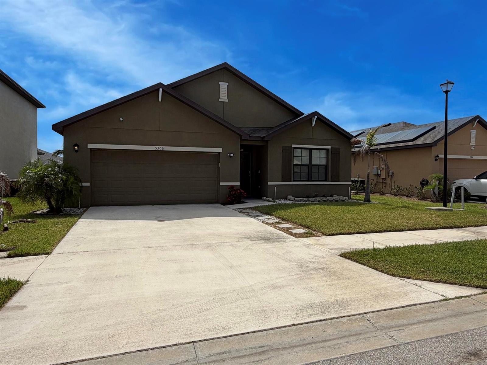 A single-story house with a brown stucco exterior, a two-car garage, and a front lawn — 5306 Entertainment Way, Fort Pierce FL 34947, FORT PIERCE, FL