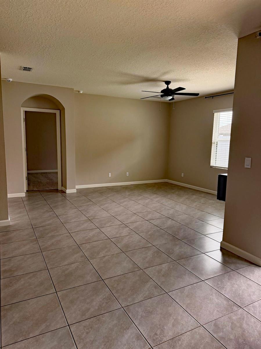 An empty room with beige walls, tile flooring, a ceiling fan, and an arched doorway — 5306 Entertainment Way, Fort Pierce FL 34947, FORT PIERCE, FL