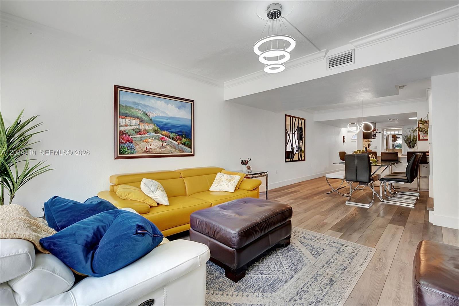 A living room with a yellow sofa, dark ottoman, and dining area on wood floors — 1187 NW 123rd Pl, Miami FL 33182, MIAMI, FL