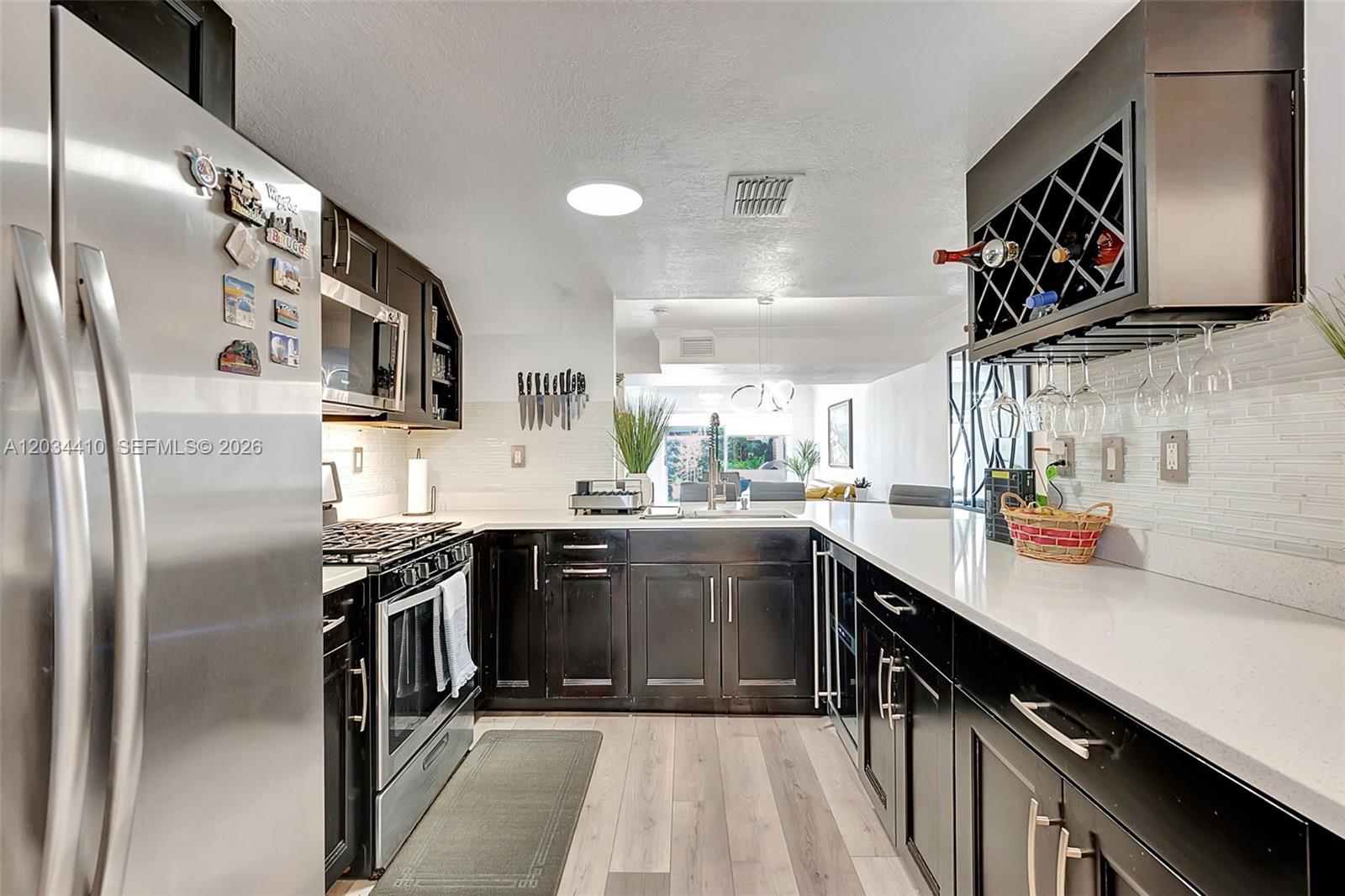 A modern kitchen features dark cabinetry, stainless steel appliances, and white countertops — 1187 NW 123rd Pl, Miami FL 33182, MIAMI, FL