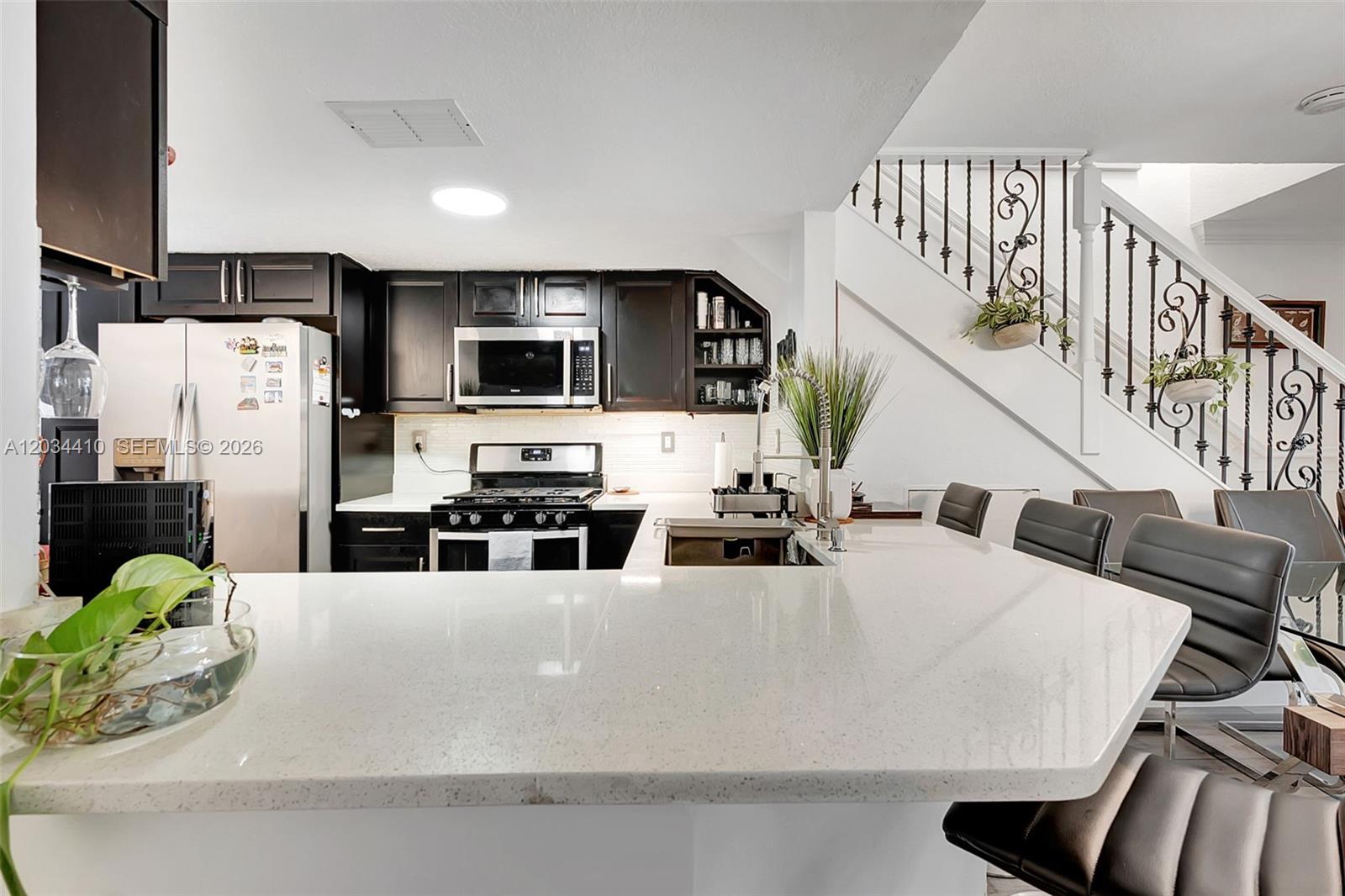 A kitchen features dark cabinets, white countertops, a breakfast bar, and a staircase with railing — 1187 NW 123rd Pl, Miami FL 33182, MIAMI, FL