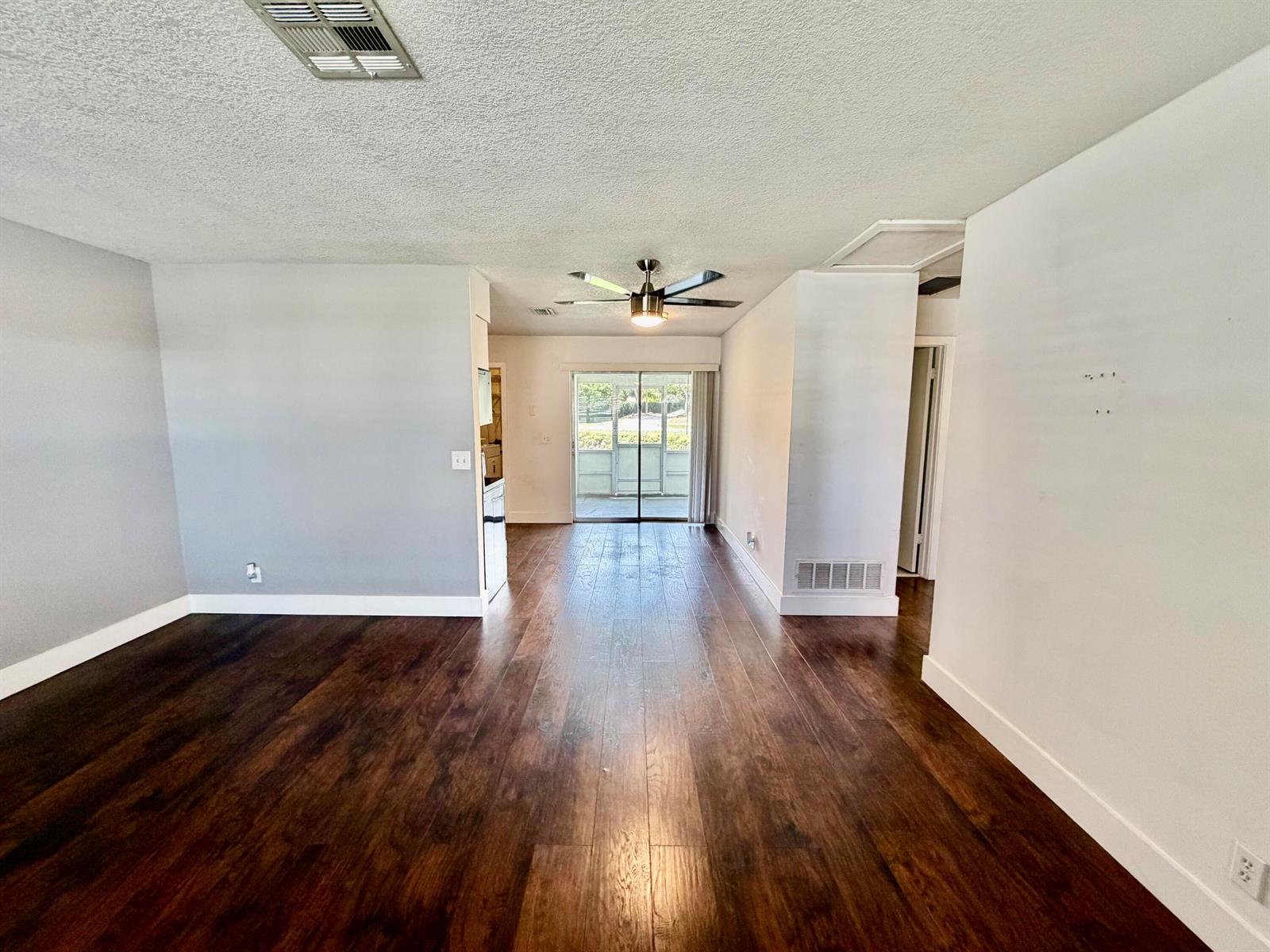 An empty living room features dark wood-look flooring, white walls, and a ceiling fan — 2821 Duke Lane, Delray Beach FL 33445, DELRAY BEACH, FL