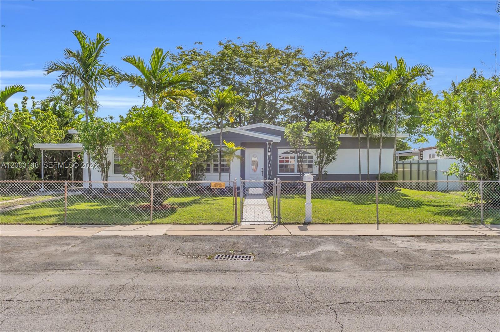 A single-story house with a white and gray exterior sits behind a chain-link fence — 5971 W 13th Ave, Hialeah FL 33012, HIALEAH, FL