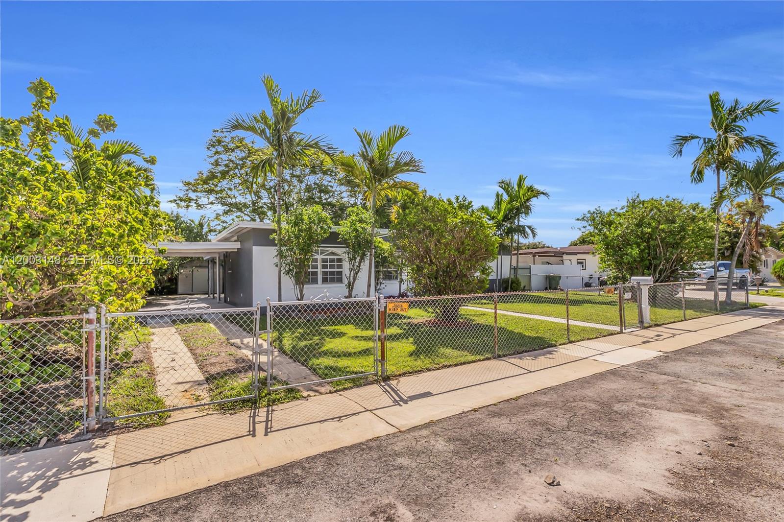 A single-story house with a carport and chain-link fence sits on a grassy lot — 5971 W 13th Ave, Hialeah FL 33012, HIALEAH, FL