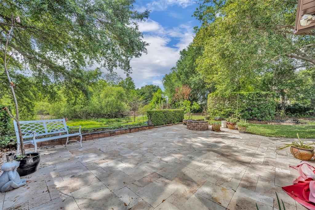 A stone patio features a white bench, a brick fire pit, and surrounding lush trees — 13536 SUNSET LAKES CIRCLE, WINTER GARDEN, FL