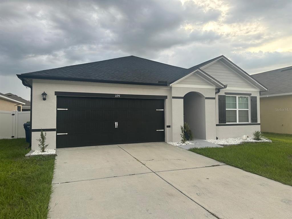 A single-story house with a two-car garage, light stucco walls, and dark trim — 1199 SOPHIA BOULEVARD, WINTER HAVEN, FL