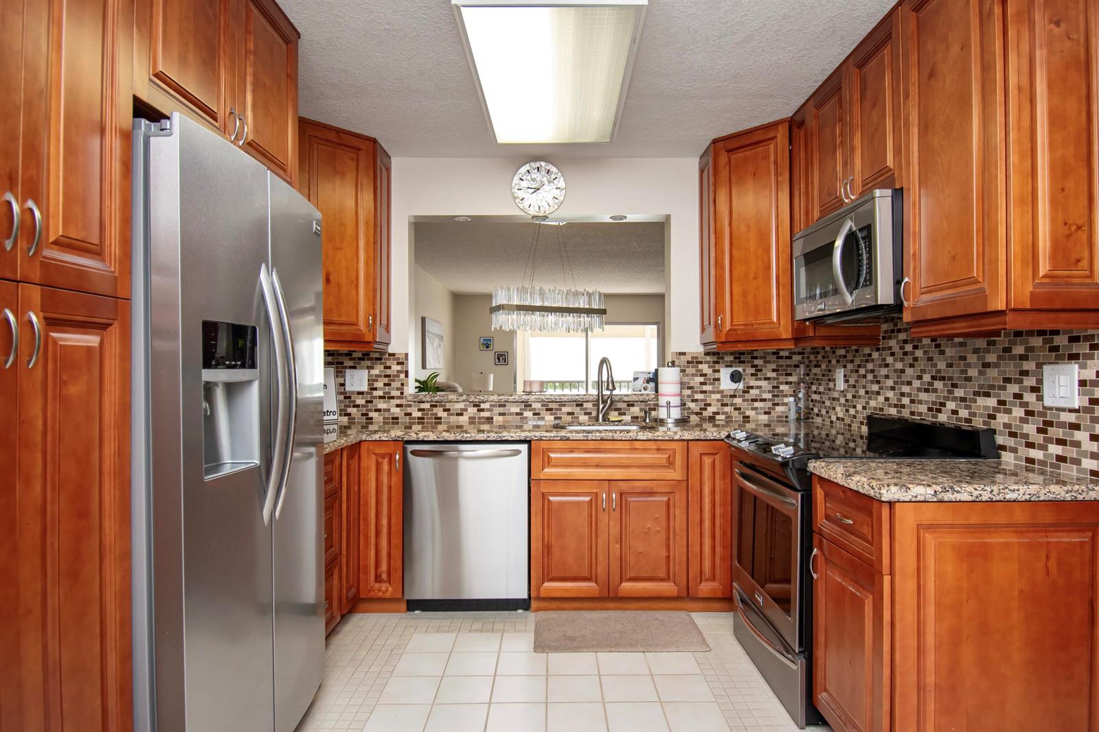 A kitchen with wood cabinets, stainless steel appliances, granite countertops, and a tiled backsplash — 7286 Huntington Lane # 408, Delray Beach FL 33446, DELRAY BEACH, FL
