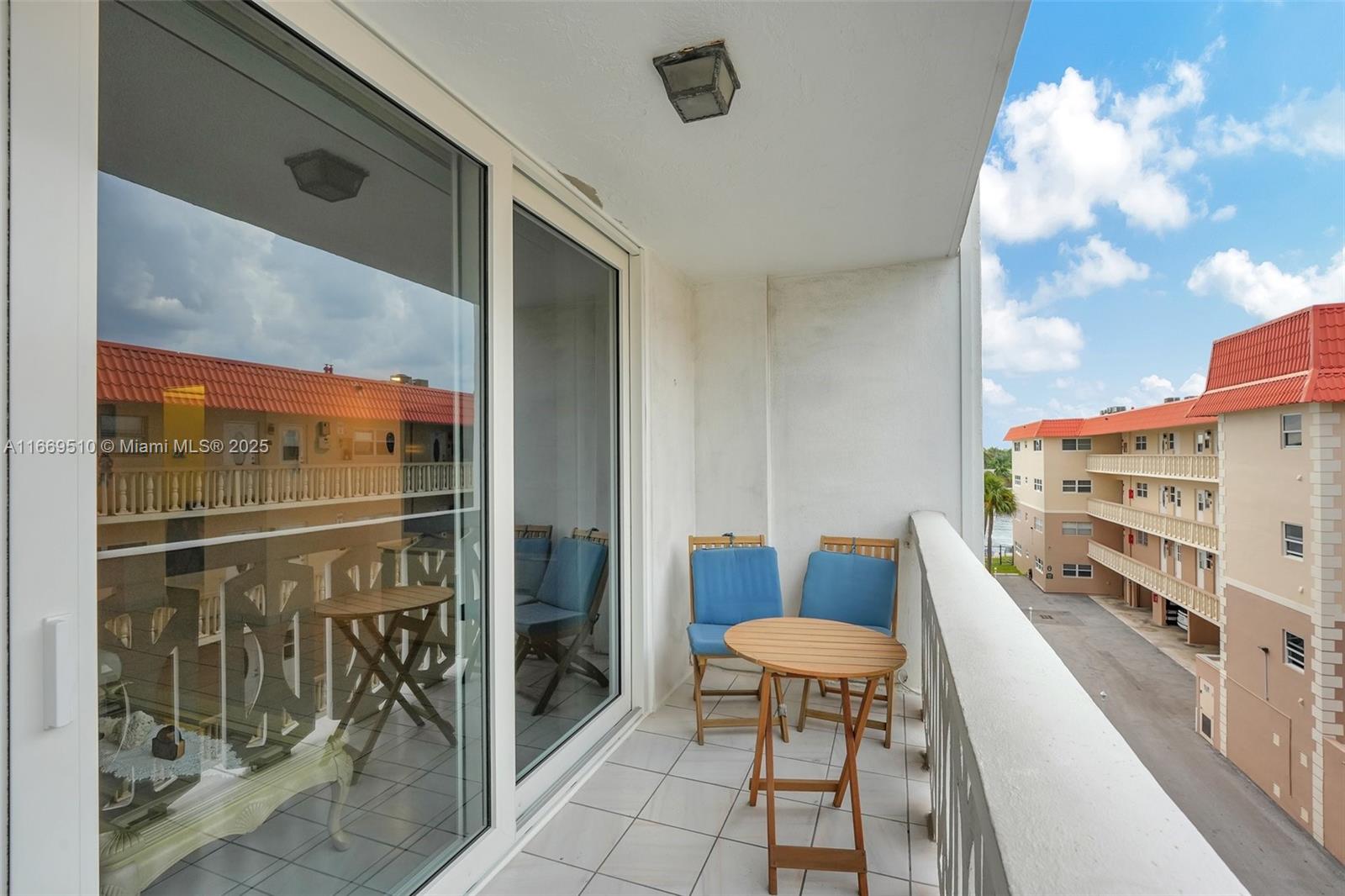 A balcony with white tile flooring, two blue chairs, and a small wooden table — 3113 S Ocean Dr # 402, Hallandale Beach FL 33009, HALLANDALE BEACH, FL