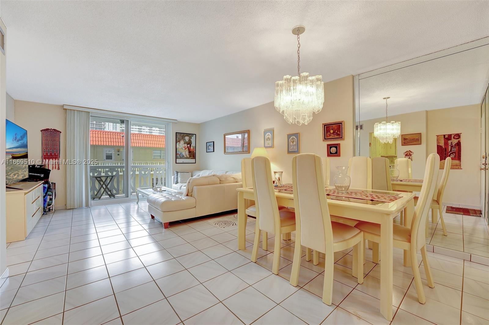A bright living and dining area features white tile floors, a crystal chandelier, and a balcony — 3113 S Ocean Dr # 402, Hallandale Beach FL 33009, HALLANDALE BEACH, FL