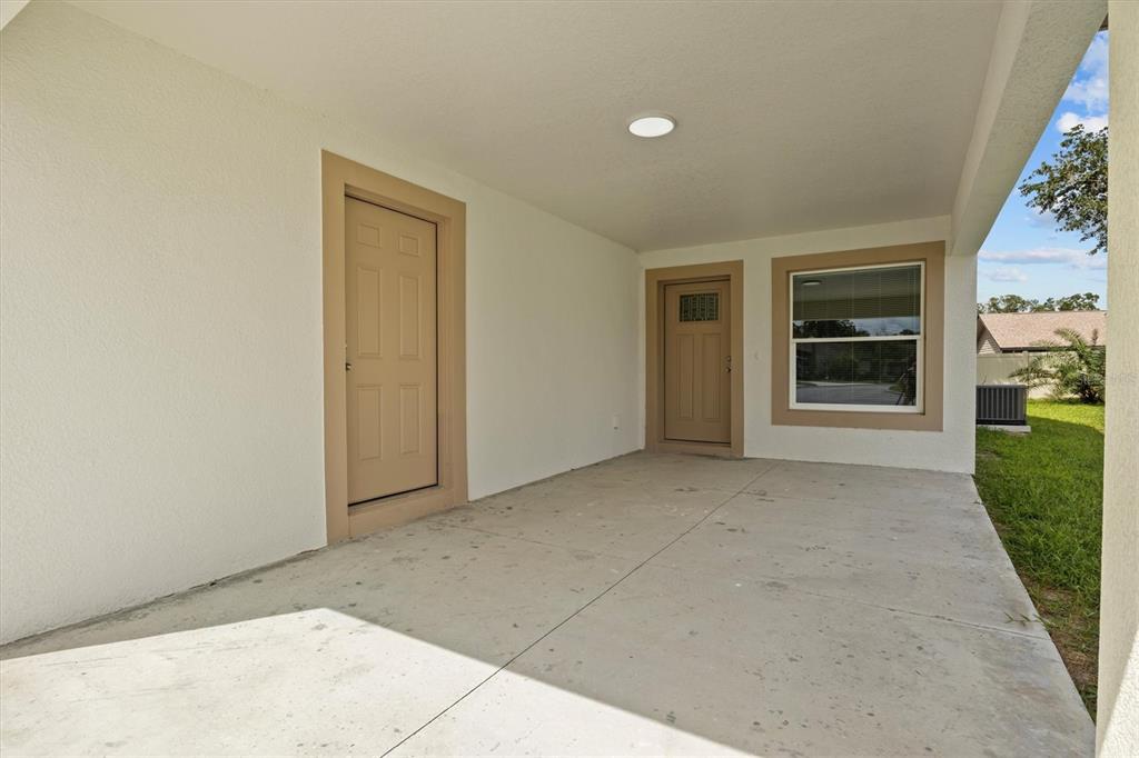 A covered concrete patio features two tan doors and a window on a white wall — 4078 OAK LOOP, MULBERRY, FL