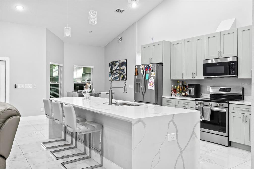 A modern kitchen features a large white marble-topped island, gray cabinetry, and stainless steel appliances — 14112 LORD BARCLAY DRIVE, ORLANDO, FL