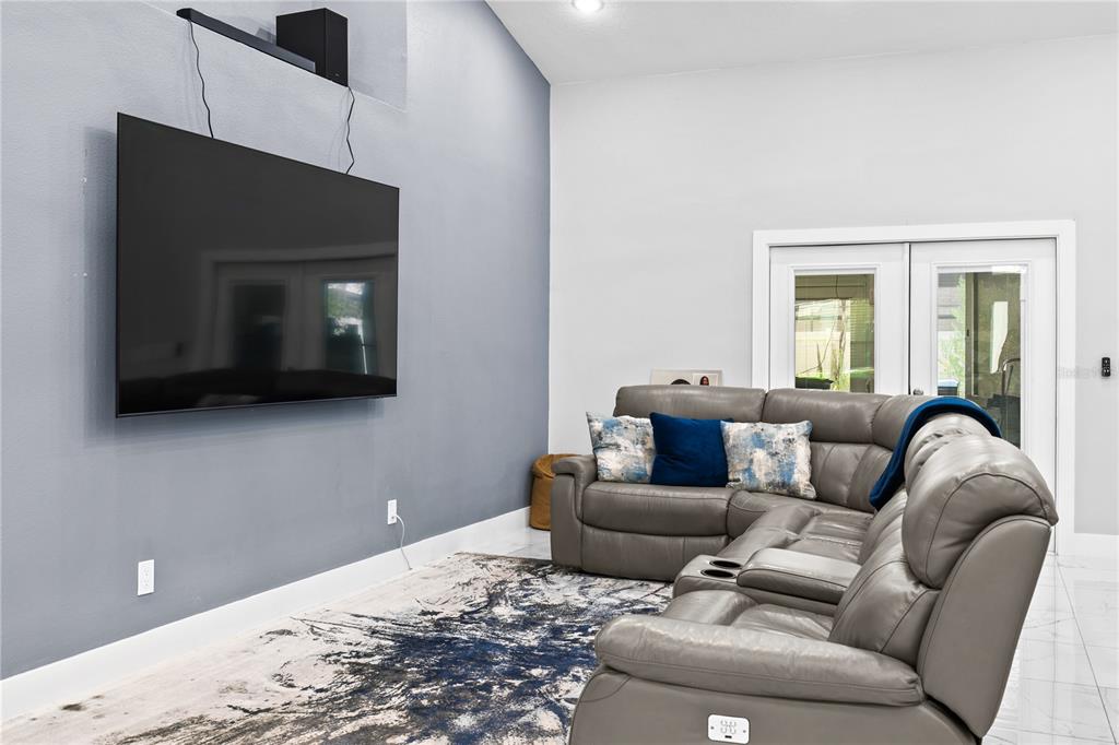 A living room features a large wall-mounted television, a grey sectional sofa, and tile flooring — 14112 LORD BARCLAY DRIVE, ORLANDO, FL