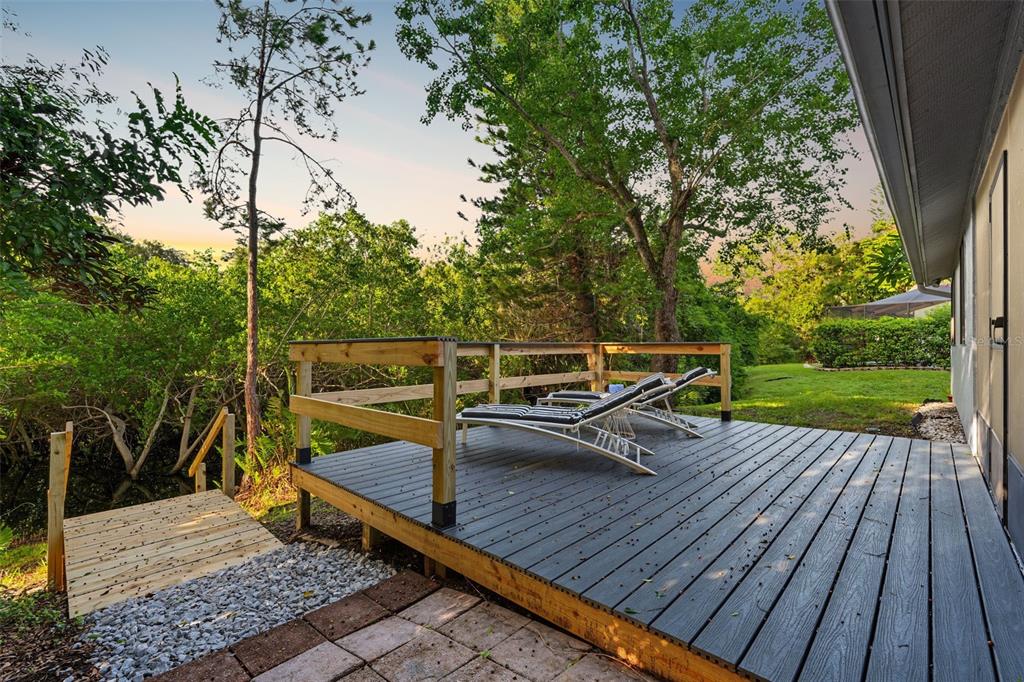 A wooden deck with two lounge chairs overlooks a wooded area and a small pond — 3010 LONGBROOKE WAY, CLEARWATER, FL