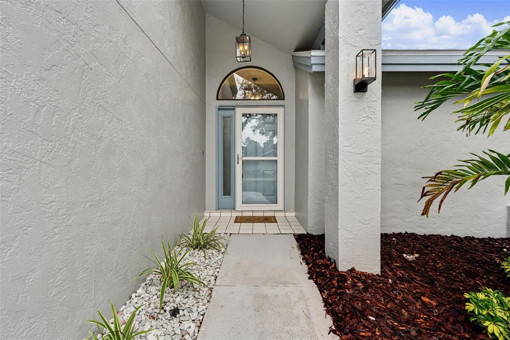 A concrete walkway leads to the front entrance of a house with a glass door — 3010 LONGBROOKE WAY, CLEARWATER, FL