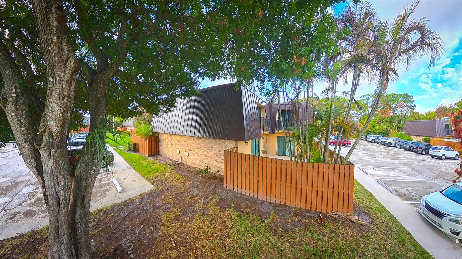 An exterior view of a two-story apartment building with a brown mansard roof and fence — 5646 SE Windsong Lane # 415, Stuart FL 34997, STUART, FL