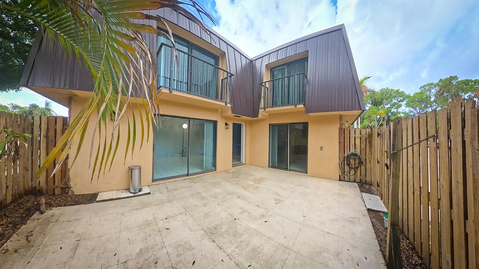 A two-story house exterior features a concrete patio, sliding glass doors, and upper-level balconies — 5646 SE Windsong Lane # 415, Stuart FL 34997, STUART, FL