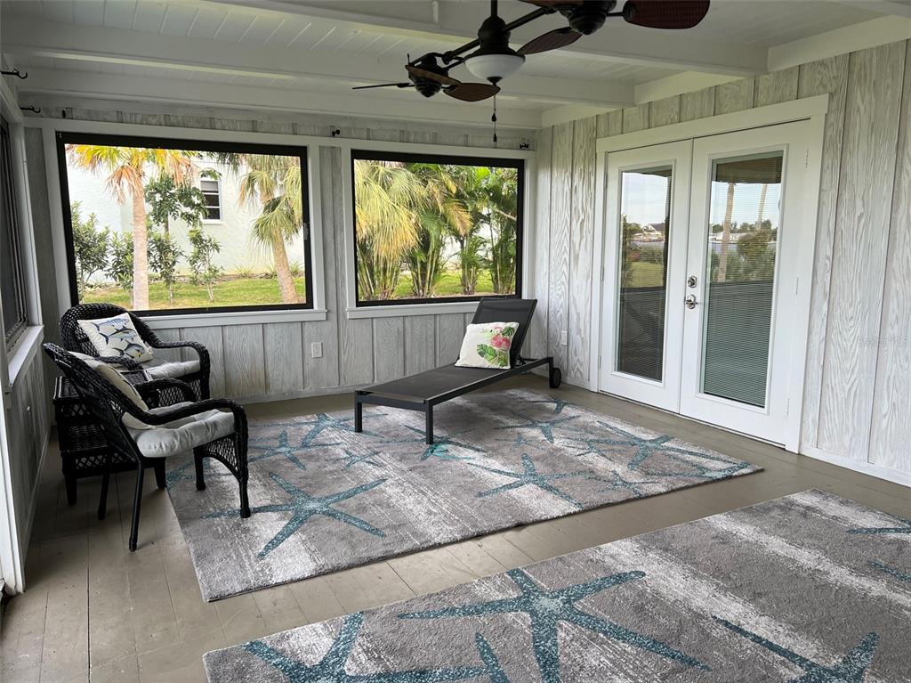 A sunroom features a ceiling fan, two wicker chairs, a lounge chair, and starfish-patterned rugs — 1626 NEW POINT COMFORT ROAD, ENGLEWOOD, FL