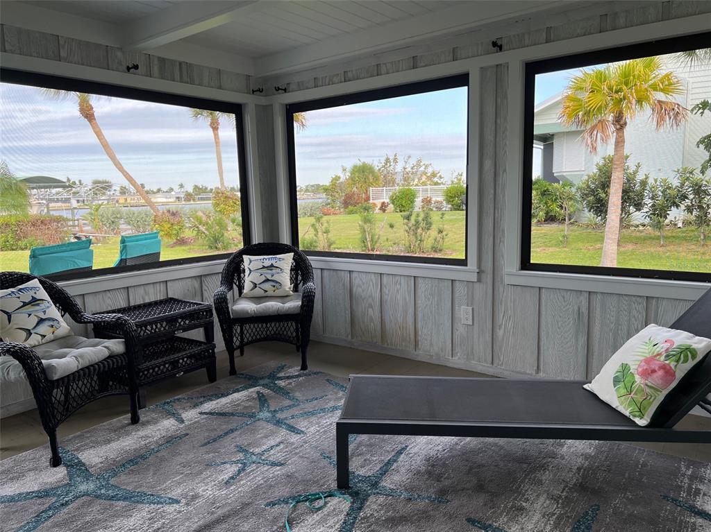 A screened-in porch features wicker furniture, a starfish-patterned rug, and views of a waterfront yard — 1626 NEW POINT COMFORT ROAD, ENGLEWOOD, FL