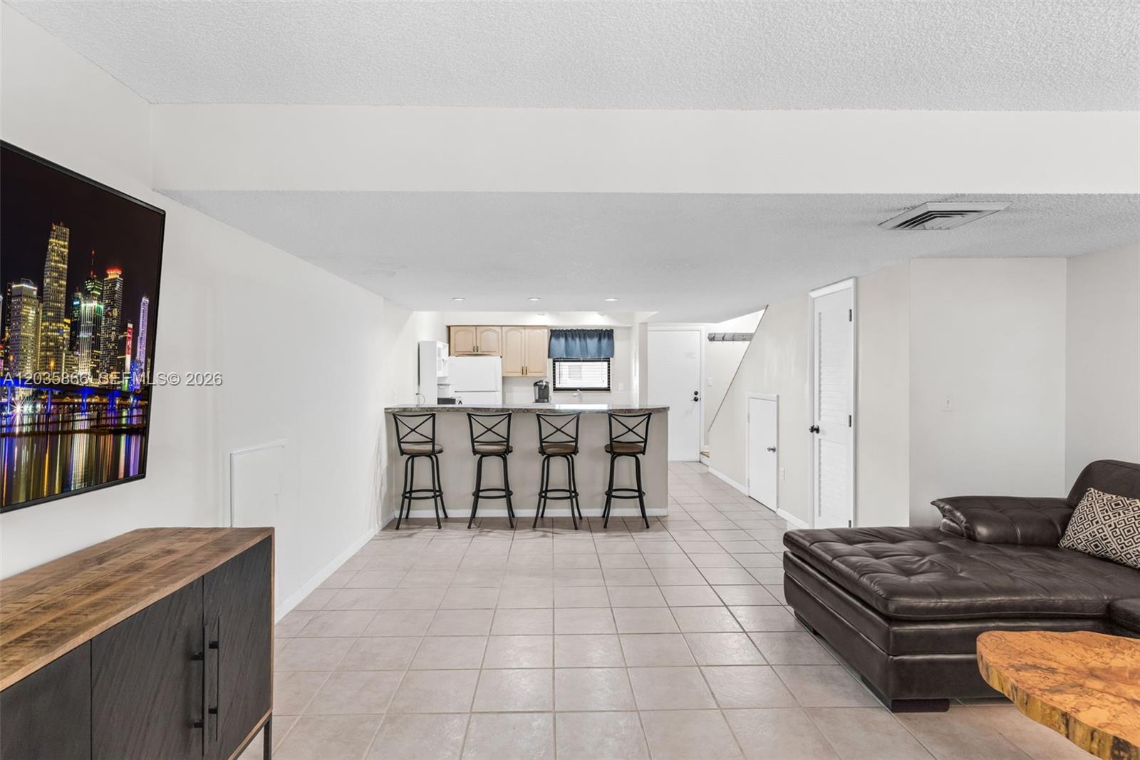A living room with tile flooring features a breakfast bar, kitchen, and wall-mounted television — 87455 Old Hwy # 247, Islamorada FL 33036, ISLAMORADA, FL