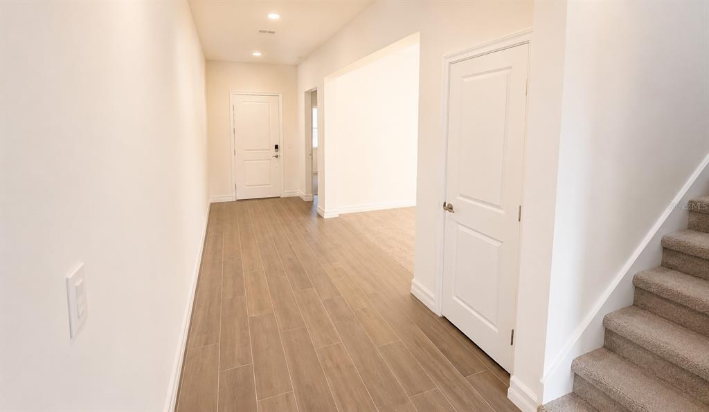 A bright entryway features wood-look tile flooring, a white door, and carpeted stairs — 12558 COLONNADE VISTA DRIVE, RIVERVIEW, FL