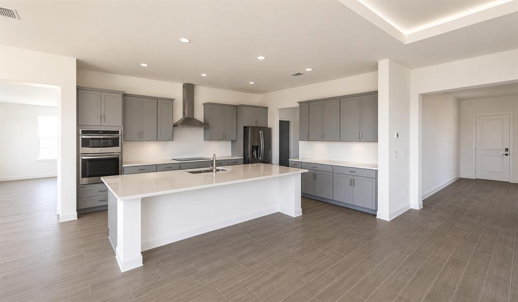 A modern kitchen features gray cabinets, white countertops, a large island, and stainless steel appliances — 12558 COLONNADE VISTA DRIVE, RIVERVIEW, FL