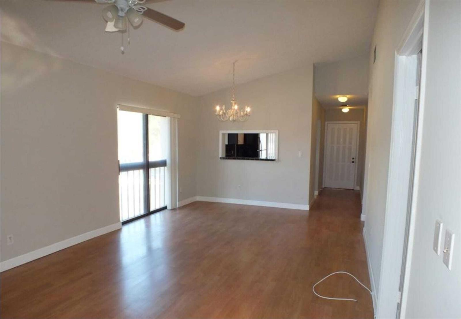 An empty living room with wood-look flooring, a ceiling fan, and a chandelier — 300 E Club Circle # 201, Boca Raton FL 33487, BOCA RATON, FL