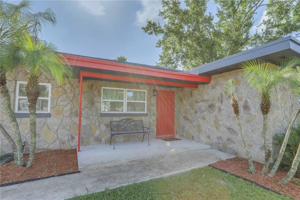 The exterior of a stone-faced house features a red front door and a covered porch — 121 S TRIPLET LAKE DRIVE, CASSELBERRY, FL