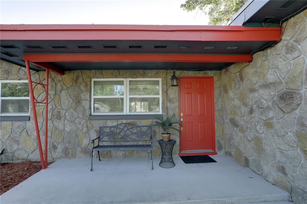 A stone-clad house exterior features a bright red front door, a bench, and a porch — 121 S TRIPLET LAKE DRIVE, CASSELBERRY, FL
