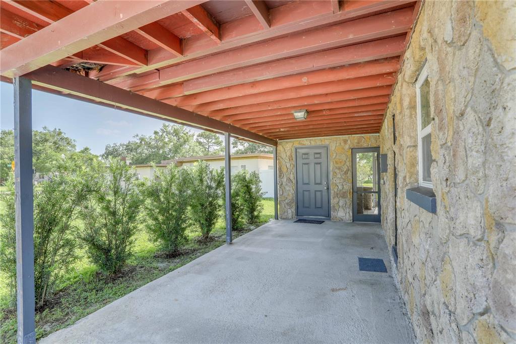 A covered concrete patio features a stone exterior wall and a red wooden ceiling — 121 S TRIPLET LAKE DRIVE, CASSELBERRY, FL
