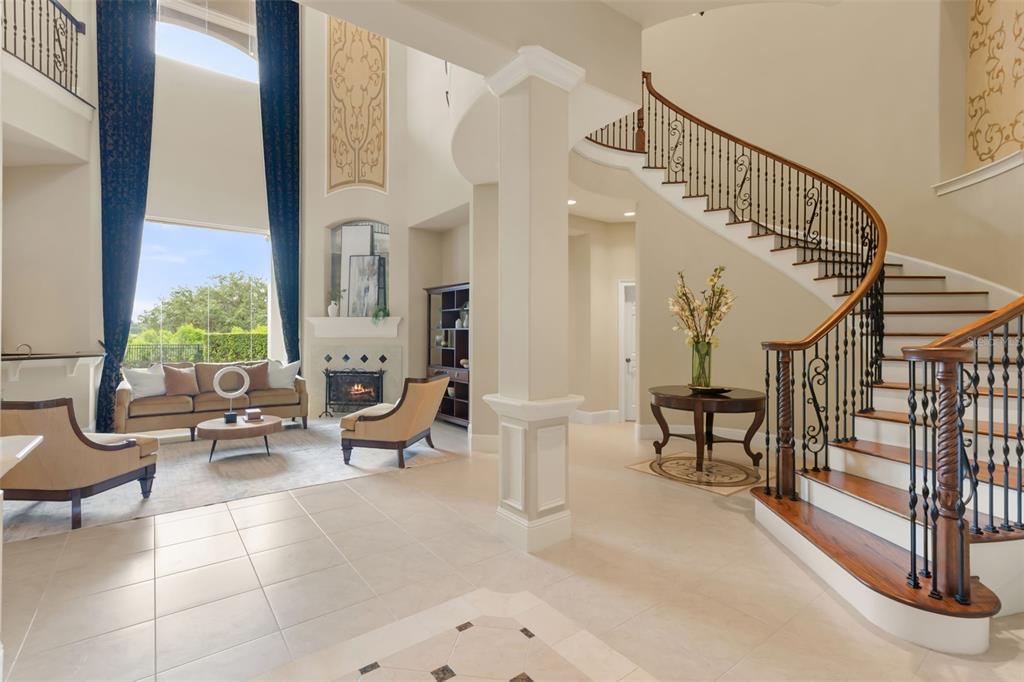 A grand foyer features a curved staircase, tile flooring, and an open living area beyond — 26010 ESTATES RIDGE DRIVE, SORRENTO, FL