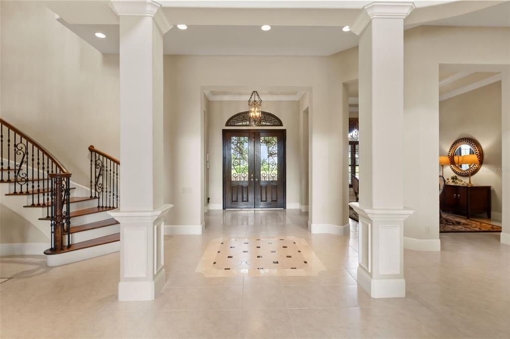 A grand foyer features a curved staircase, tile flooring with an inlay, and double doors — 26010 ESTATES RIDGE DRIVE, SORRENTO, FL