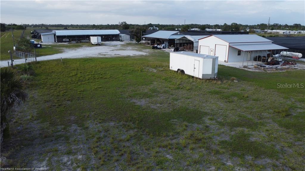 An aerial view shows a grassy lot with a white trailer and several metal buildings — 300 SR-70 E, LAKE PLACID, FL