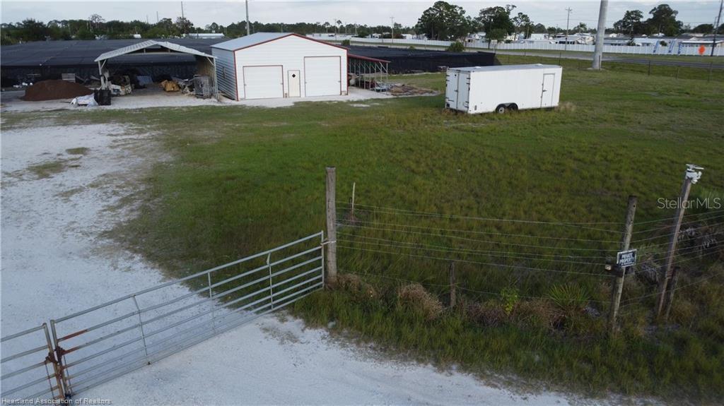 An aerial view shows a fenced lot with a white garage, a trailer, and structures — 300 SR-70 E, LAKE PLACID, FL