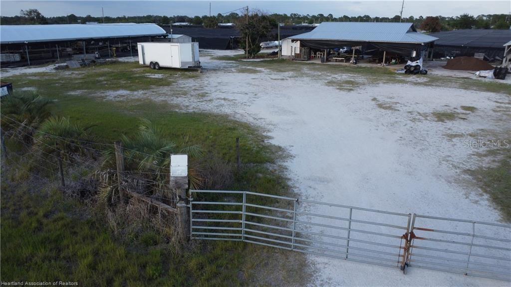 An aerial view shows a gravel lot with a metal gate, trailer, and open-sided structures — 300 SR-70 E, LAKE PLACID, FL
