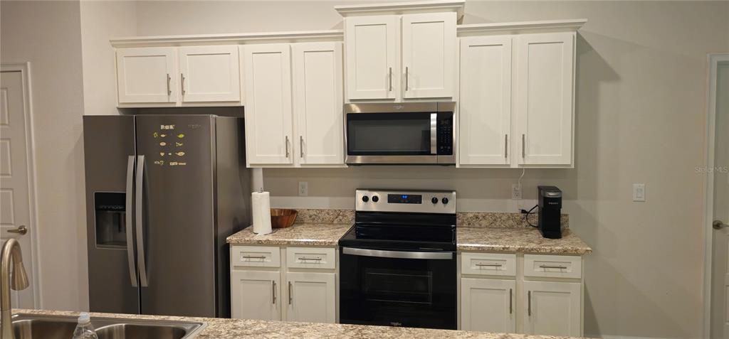 A kitchen features white cabinets, stainless steel appliances, and speckled granite countertops — 137 ULLIAN TRAIL, PALM COAST, FL