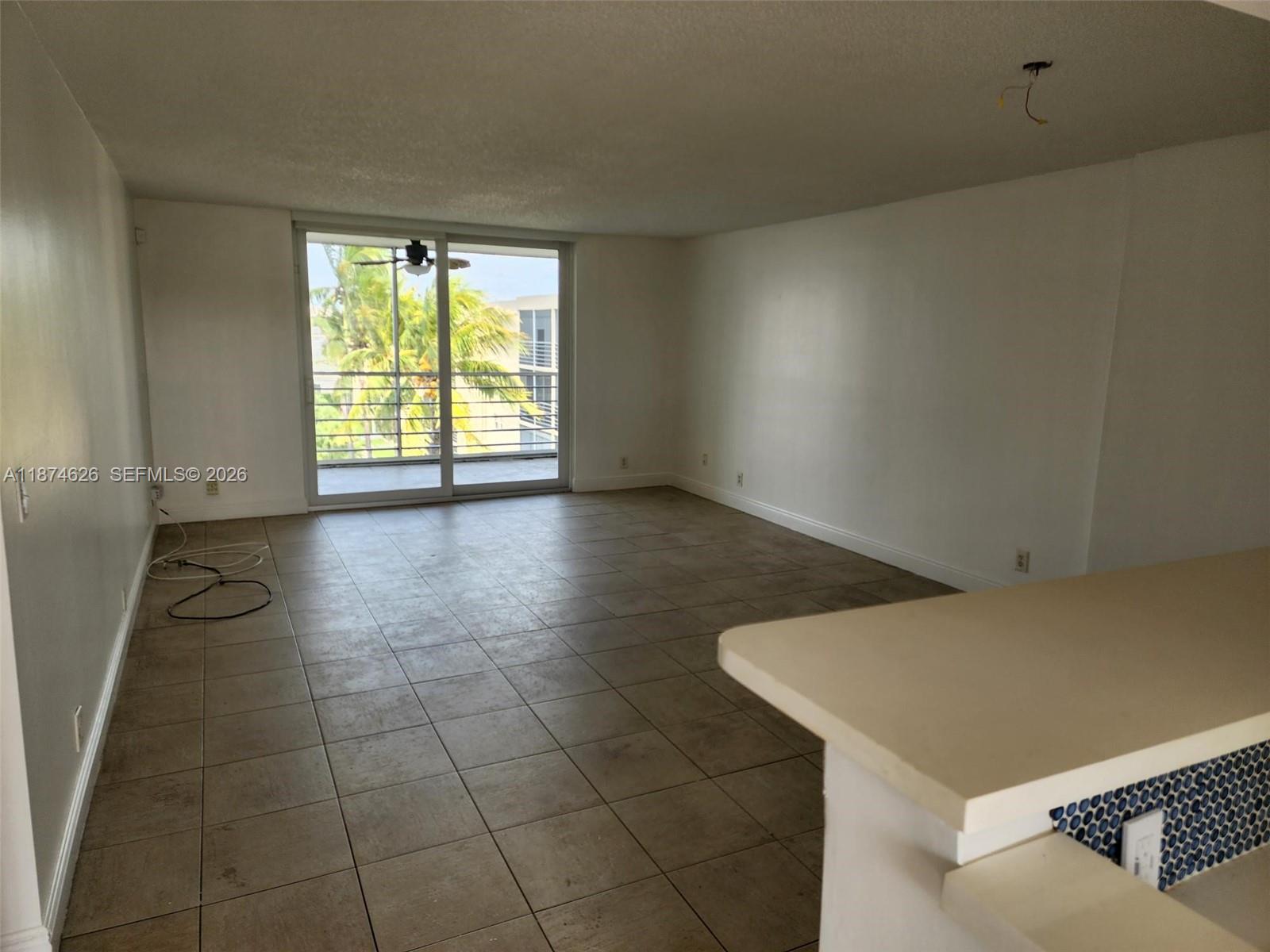 An empty living room features beige tile flooring, white walls, and a sliding glass balcony door — 425 SE 11th Ter # 403, Dania Beach FL 33004, DANIA BEACH, FL