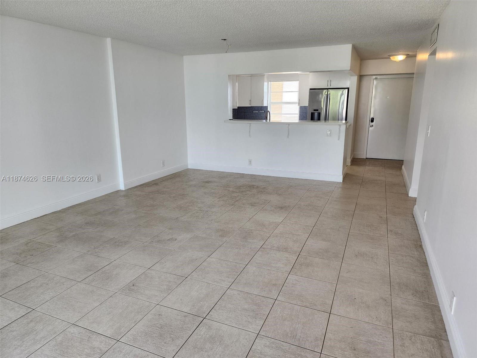 An open-concept living area features light-colored floor tiles, white walls, and a kitchen pass-through window — 425 SE 11th Ter # 403, Dania Beach FL 33004, DANIA BEACH, FL