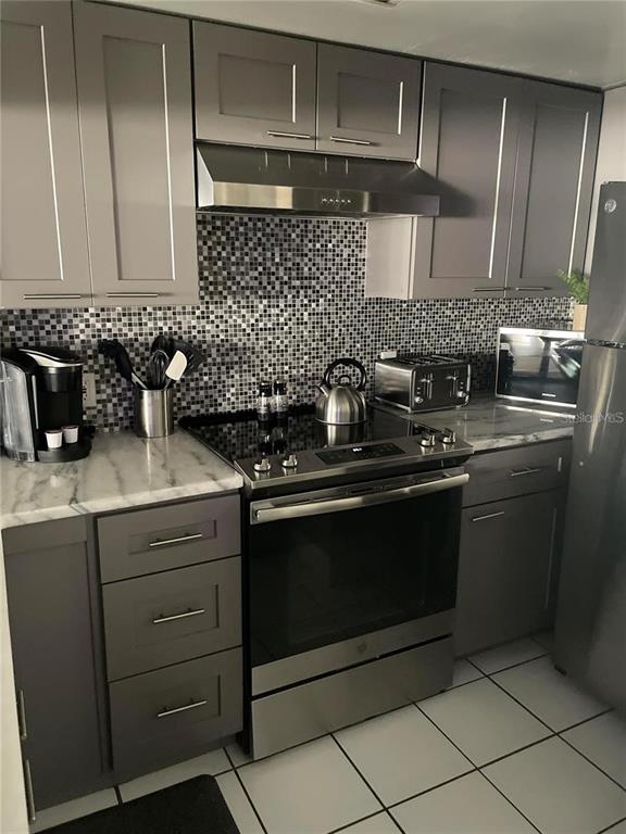 A kitchen features gray cabinets, stainless steel appliances, and a mosaic tile backsplash — 2571 CYPRUS DRIVE UNIT 1-204, PALM HARBOR, FL