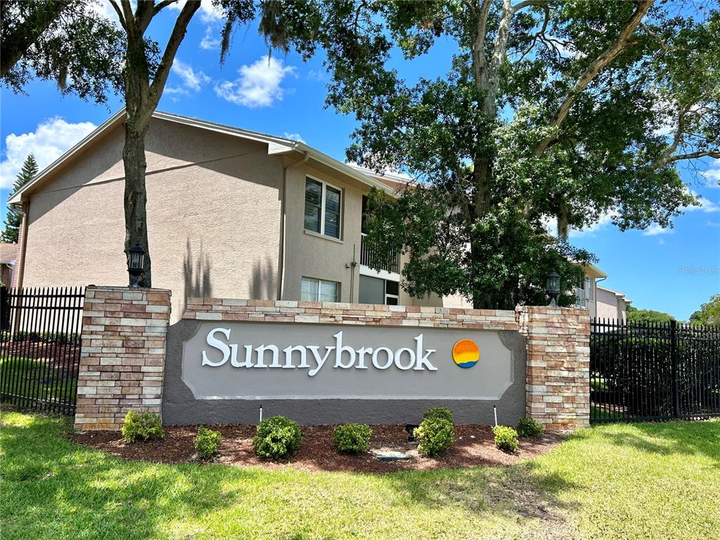 A stone monument sign for Sunnybrook stands in front of a multi-story apartment building — 6519 SPRING FLOWER DRIVE UNIT 24, NEW PORT RICHEY, FL