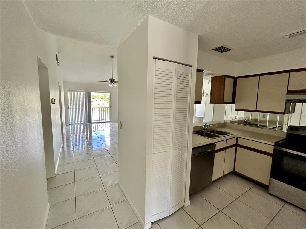 A kitchen with white cabinets and tile floors opens into a living area with balcony access — 6519 SPRING FLOWER DRIVE UNIT 24, NEW PORT RICHEY, FL