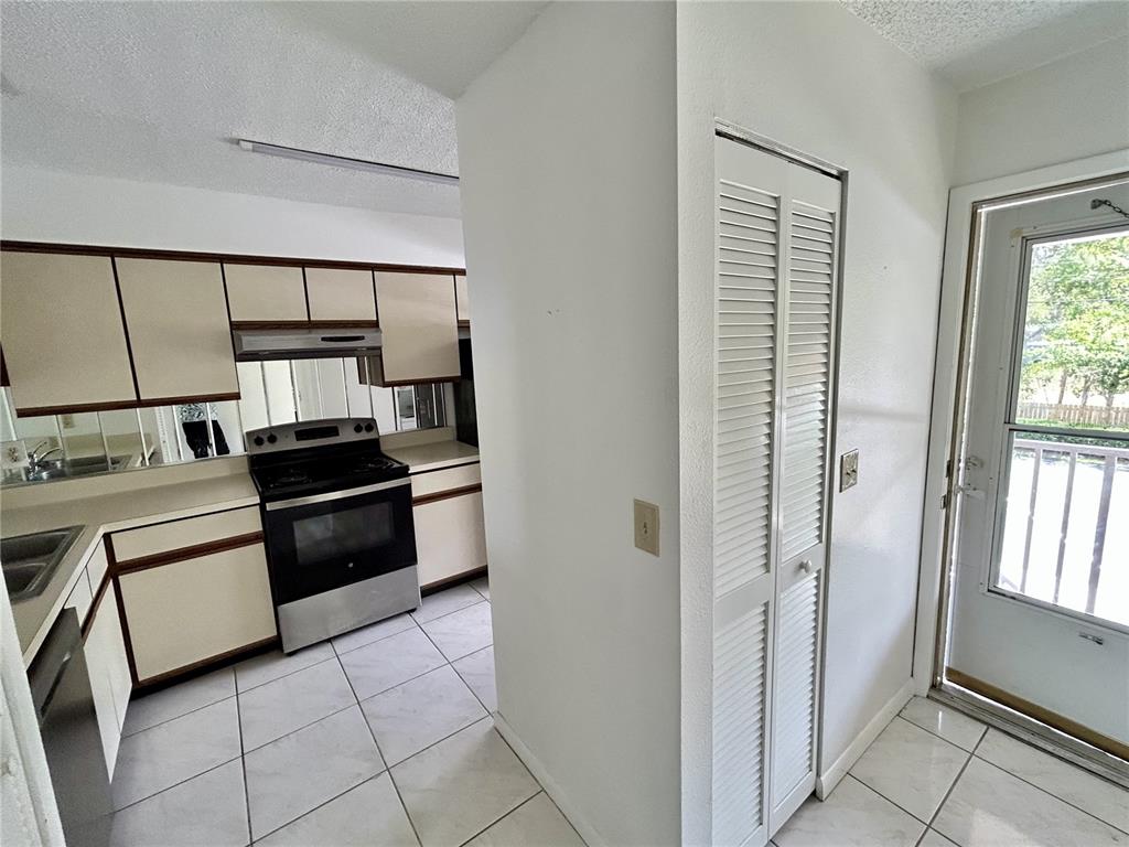 A kitchen with white cabinets, tiled floors, and a louvered door closet next to a door — 6519 SPRING FLOWER DRIVE UNIT 24, NEW PORT RICHEY, FL