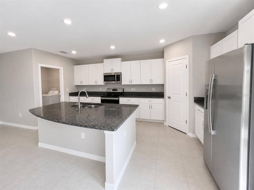 A modern kitchen features white cabinets, dark granite countertops, stainless steel appliances, and tile flooring — 16717 DELIA STREET, WIMAUMA, FL