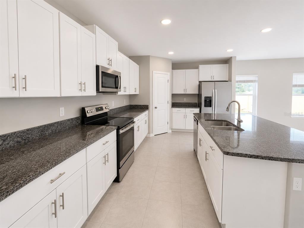 A kitchen with white cabinets, dark granite countertops, stainless steel appliances, and a central island — 16717 DELIA STREET, WIMAUMA, FL