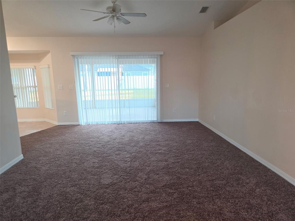 A spacious living room features brown carpeting, a ceiling fan, and sliding glass patio doors — 3 PORT LANE, PALM COAST, FL