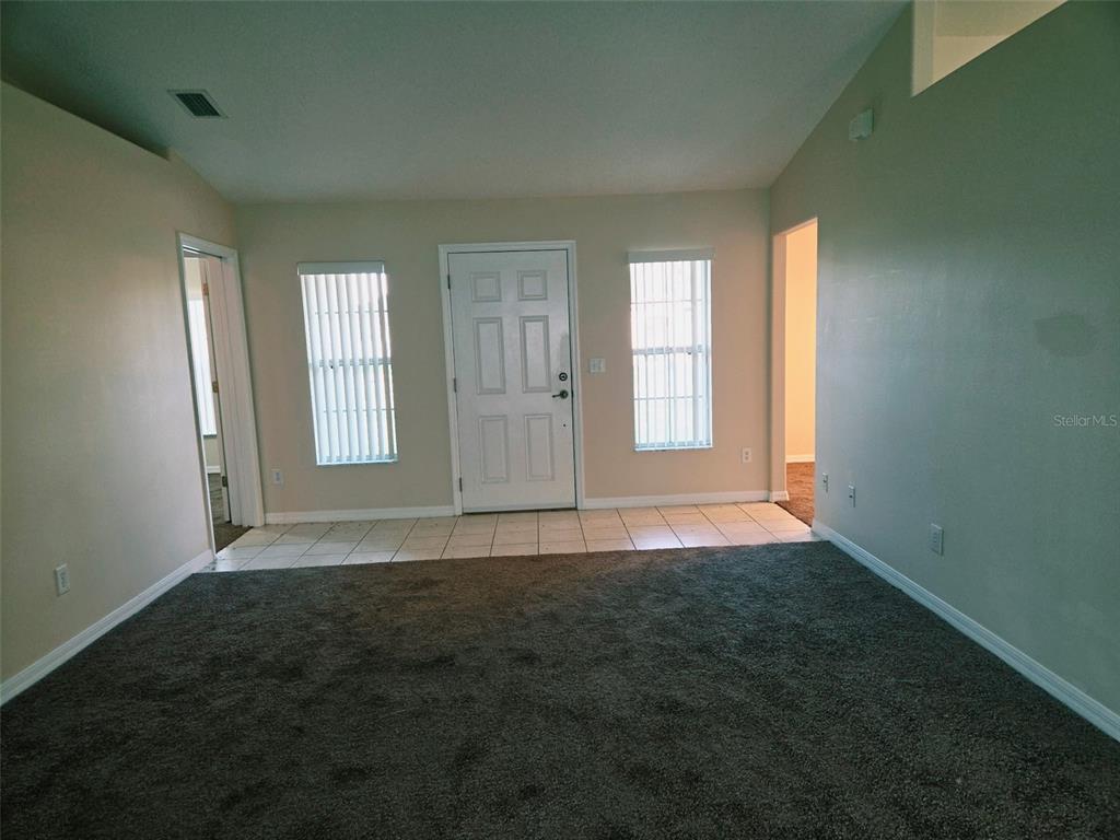 A living room features gray carpet, a tiled entryway, a front door, and two windows — 3 PORT LANE, PALM COAST, FL