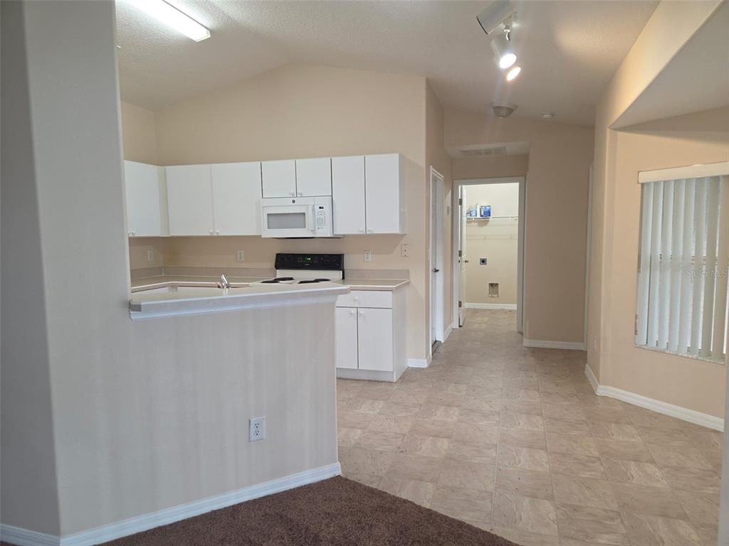 A kitchen with white cabinets, a microwave, and a tiled floor leads to a laundry room — 3 PORT LANE, PALM COAST, FL