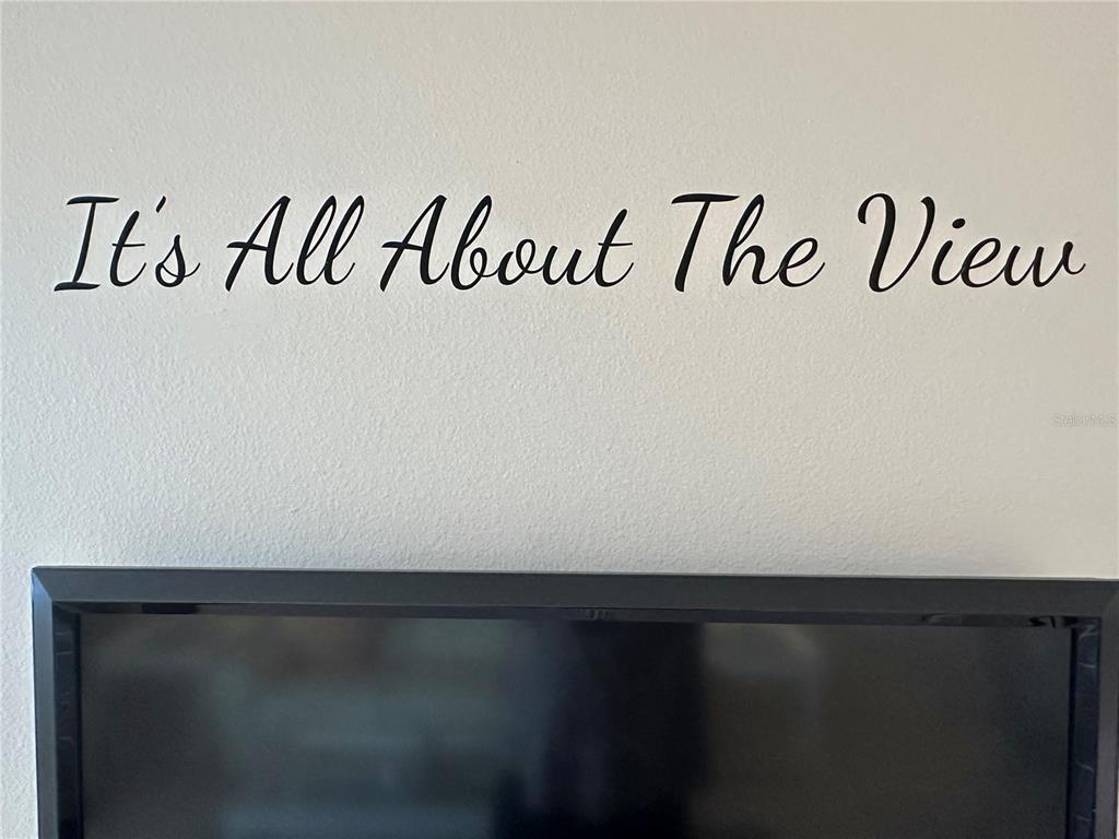 A wall decal with the text It's All About The View hangs above a television — 5915 SEA RANCH DRIVE UNIT 711, HUDSON, FL
