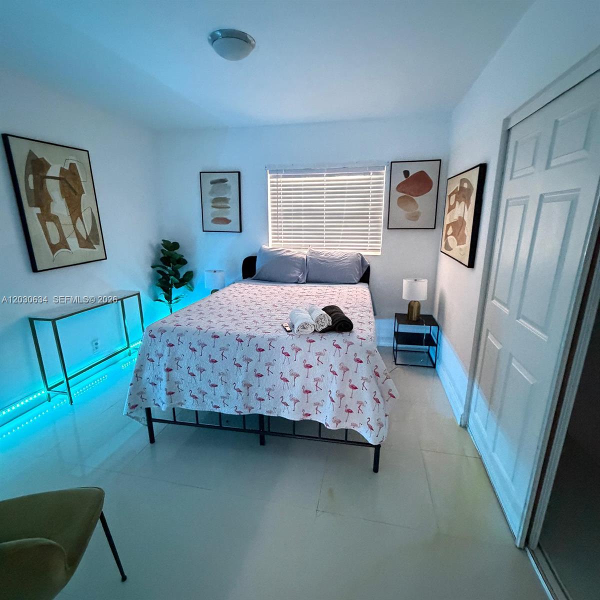 A bedroom features a bed with a flamingo-print quilt, blue accent lighting, and framed artwork — 119 SE 9th St # 12, Hallandale Beach FL 33009, HALLANDALE BEACH, FL