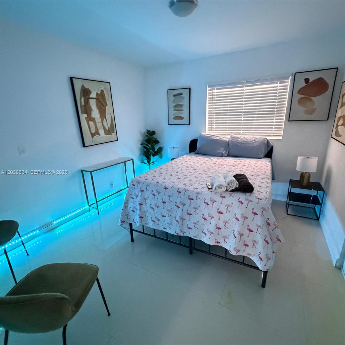 A bedroom features a flamingo-patterned bed, blue LED floor lighting, and abstract wall art — 119 SE 9th St # 12, Hallandale Beach FL 33009, HALLANDALE BEACH, FL
