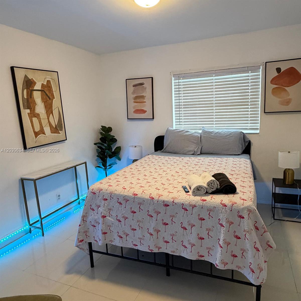 A bedroom features a flamingo-patterned bedspread, abstract wall art, and blue LED floor lighting — 119 SE 9th St # 12, Hallandale Beach FL 33009, HALLANDALE BEACH, FL